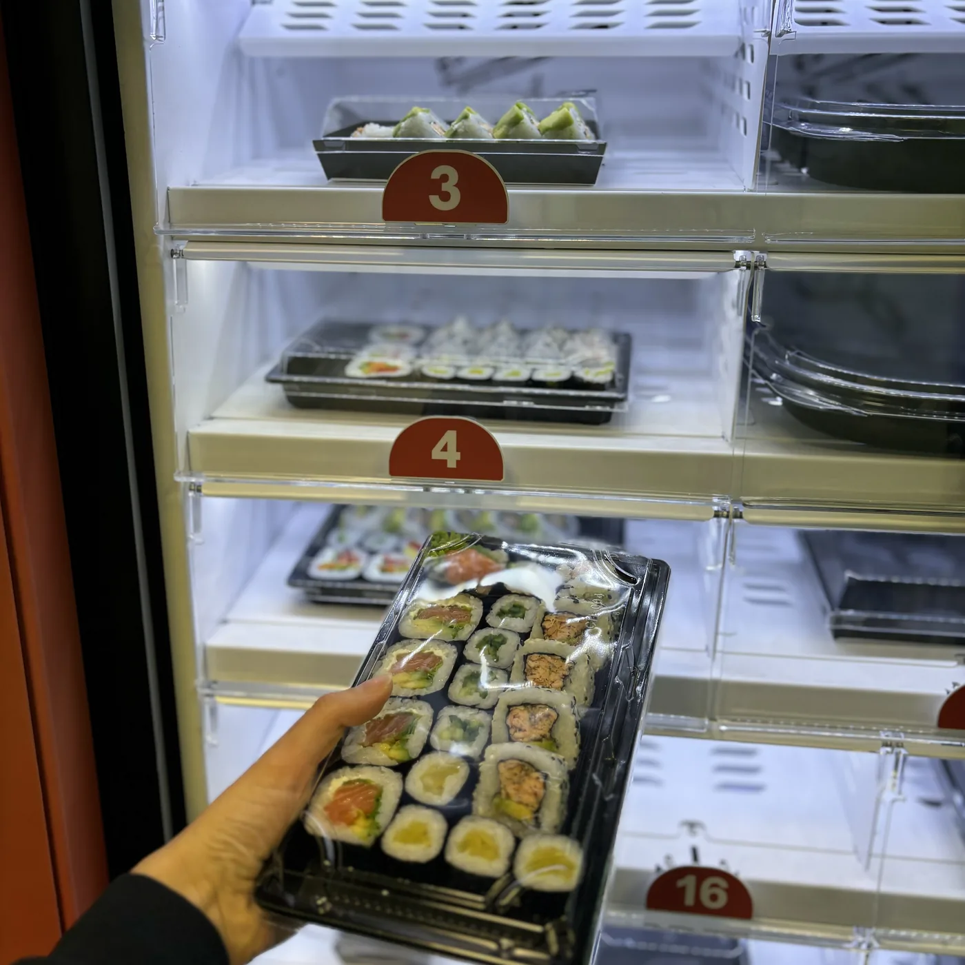 Pirkėjas atsiima sušių rinkinį iš maisto automato spintelės